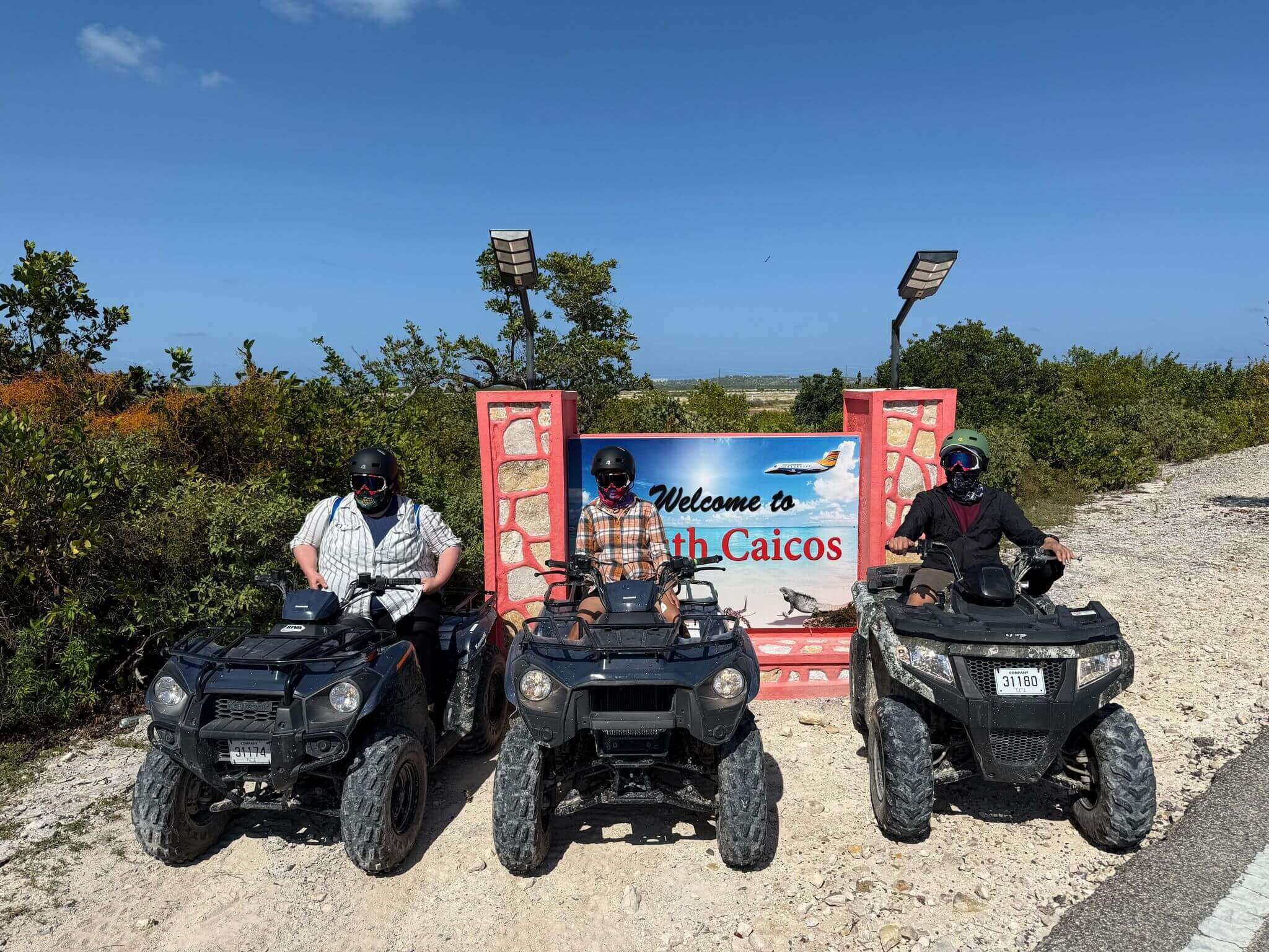 ATV riders in front of Welcome to North Caicos sign, sunny day, adventure tourism, outdoor exploration, travel destination.